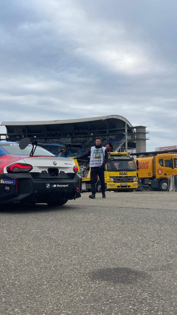 Helfer neben einem BMW-M2-Rennwagen vor der Tribüne
