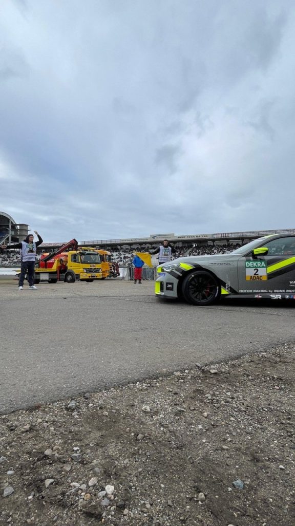 Helfer und BMW-M2-Rennwagen vor der Tribüne