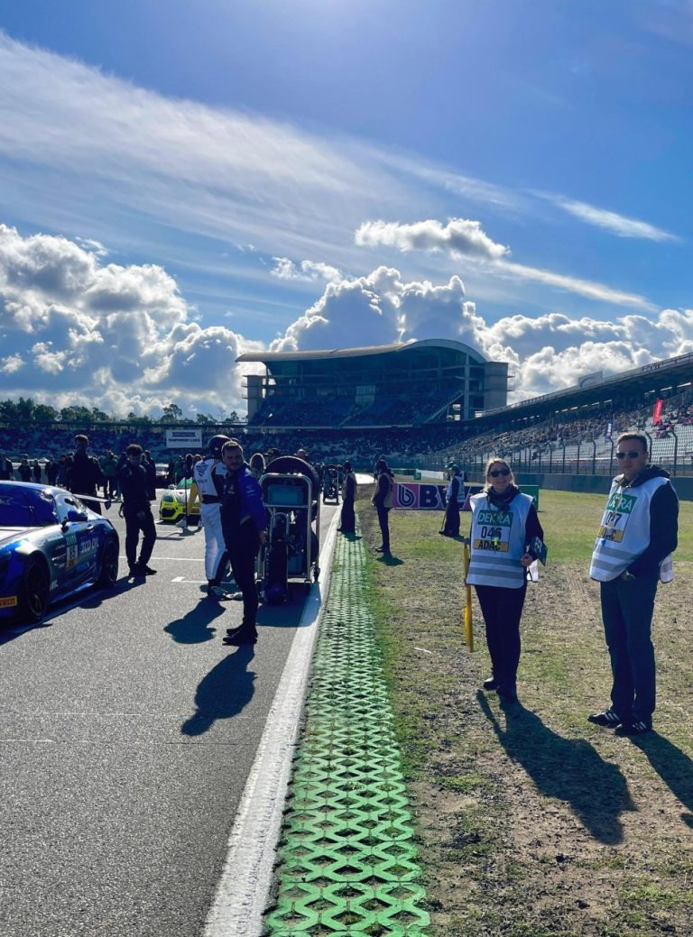 Zwei Streckenposten in Warnwesten an der Startaufstellung, im Hintergrund die Haupttribüne des Hockenheimrings