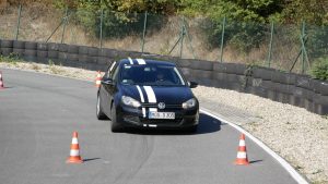 Schwarzer VW Golf mit weißen Rennstreifen beim Automobil-Slalom in Nußloch zwischen Pylonen, im Hintergrund Reifenstapel und Zaun