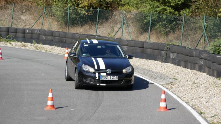 Schwarzer VW Golf mit weißen Rennstreifen beim Automobil-Slalom in Nußloch zwischen Pylonen, im Hintergrund Reifenstapel und Zaun